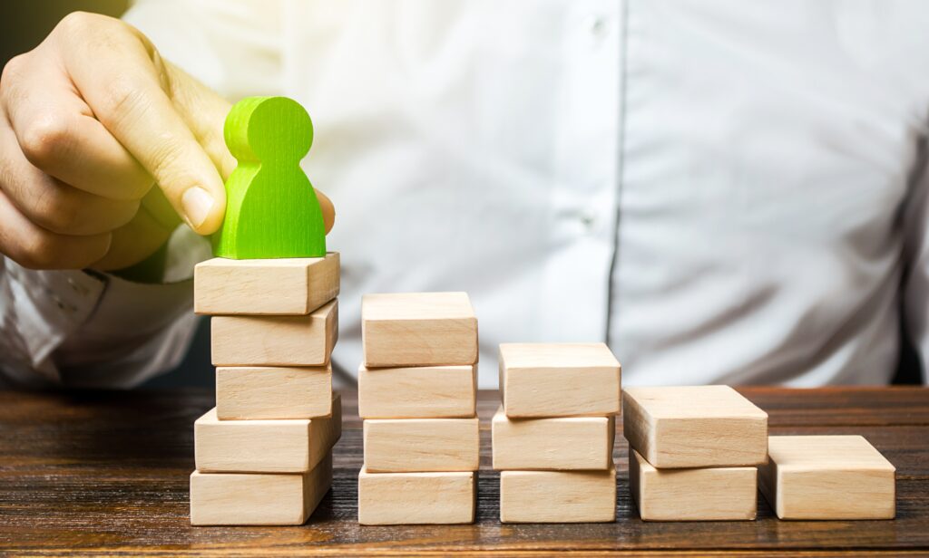 A hand placing a figure on stacked blocks, representing an employee growth plan.