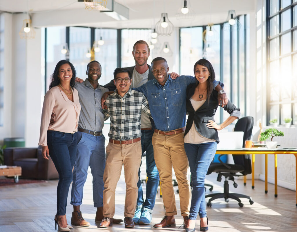 A diverse team smiling together in a modern office, addressing the question “is Newbern Excel a scam?” through workplace transparency.